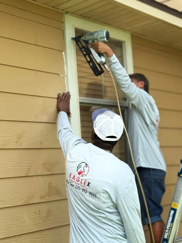 Two EagleX crew members in company shirts installing exterior trim with a nail gun