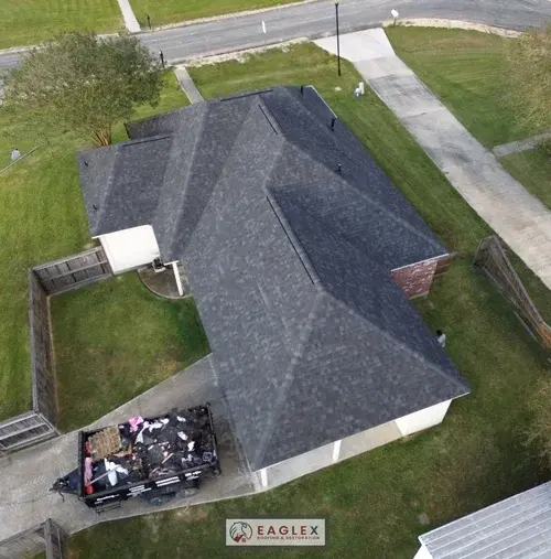 Mid-job drone aerial: new black shingle roof with a dump trailer of tear-off debris below